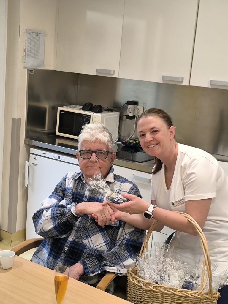 Slika prikazuje zaposleno, ki izroča manjšo pozornost slavljencu.