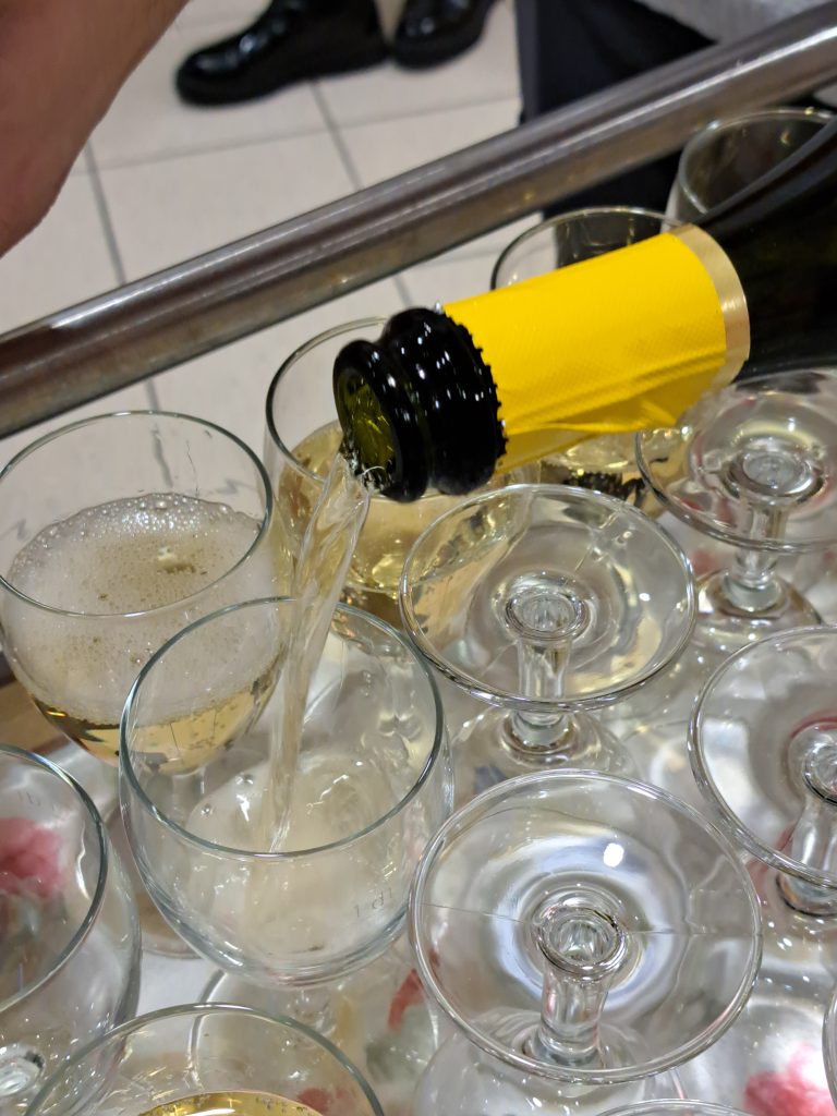 Na sliki je kozarec v katerega se naliva penina.