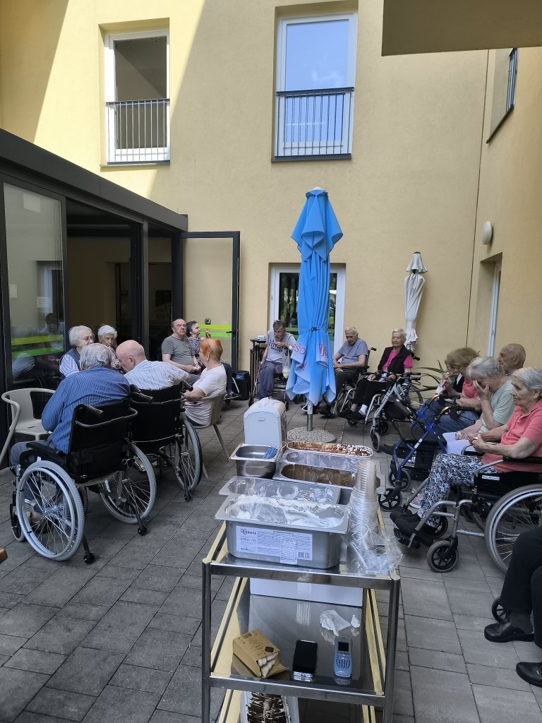 Slika prikazuje teraso kjer je množica stanovalcev, nekateri so na invalidskih vozičkih.
