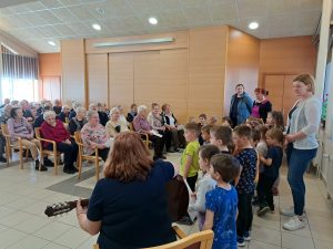 Na sliki je skupina otrok iz vrtca in skupina starejših oseb.